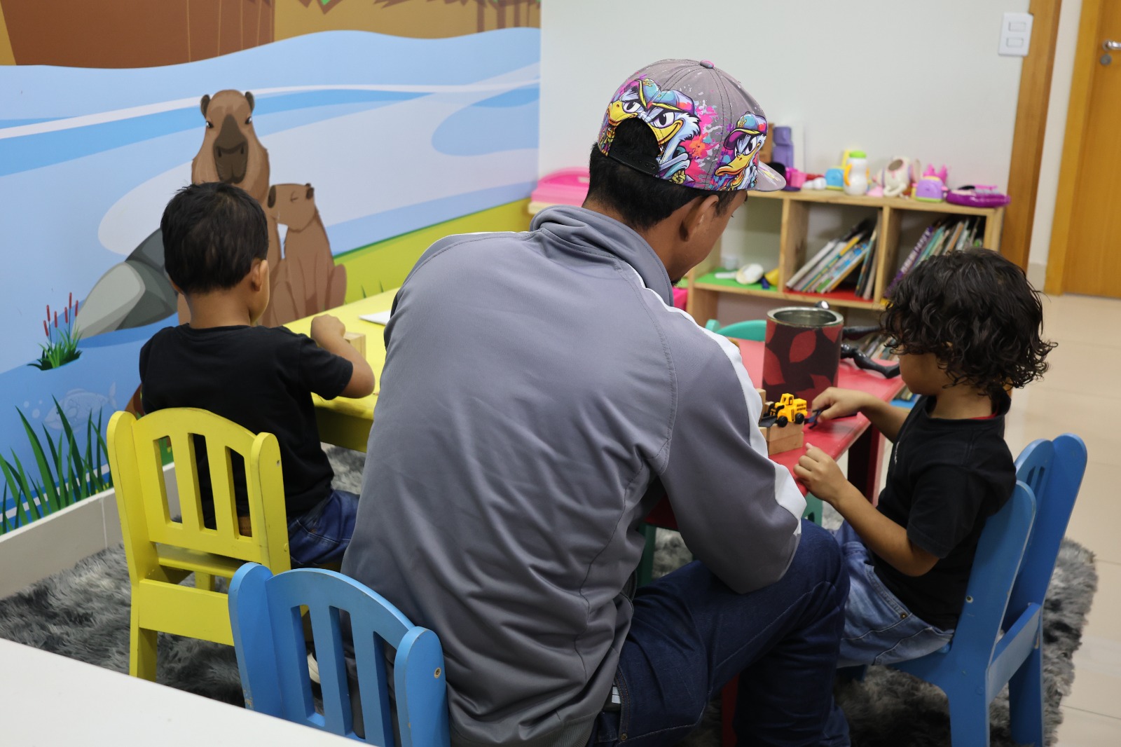 Na esperança de uma vida melhor, migrantes encontram apoio no Centro de Atendimento do Estado Crianças brincam com o pai em um espaço alegre e colorido.